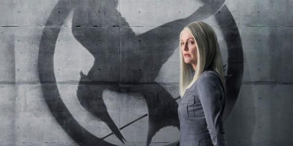 Julianne Moore as Alma Coin standing next to a wall with the Mockingjay symbol for the Hunger Games