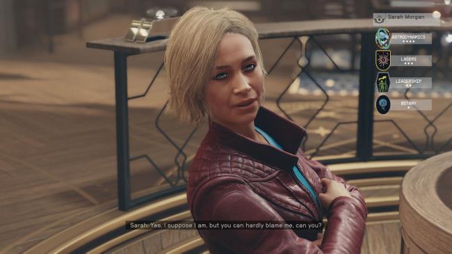 Sarah stands in the Lodge with her arms crossed.
