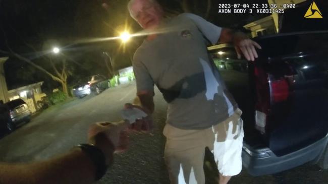 In this image from video provided by the Tampa Police Department, Joseph Ruddy, a prosecutor with the U.S. Attorney’s Office in Tampa, hands his business card to Officer Taylor Grant, outside his home in Temple Terrace, Fla., on the evening of July 4, 2023. When police arrived at his house to investigate a hit-and-run, Ruddy, one of the nation’s most prolific federal narcotics prosecutors, was so drunk he could barely stand up straight, leaning on the tailgate of his pickup to keep his balance. (Officer Taylor Grant/Tampa Police Department)