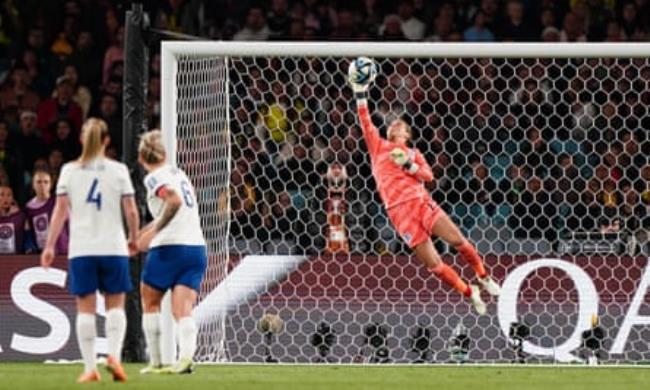 Earps diving high to her right to get one hand on the ball as two England defenders look on